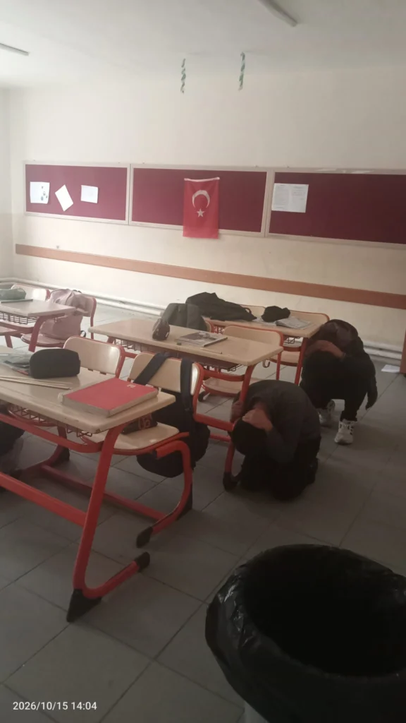 Deprem anı uygulaması sınıflarda gerçekleştirildi.
Öğrenciler sıraların yanında çömelerek tatbikata katılıyor.