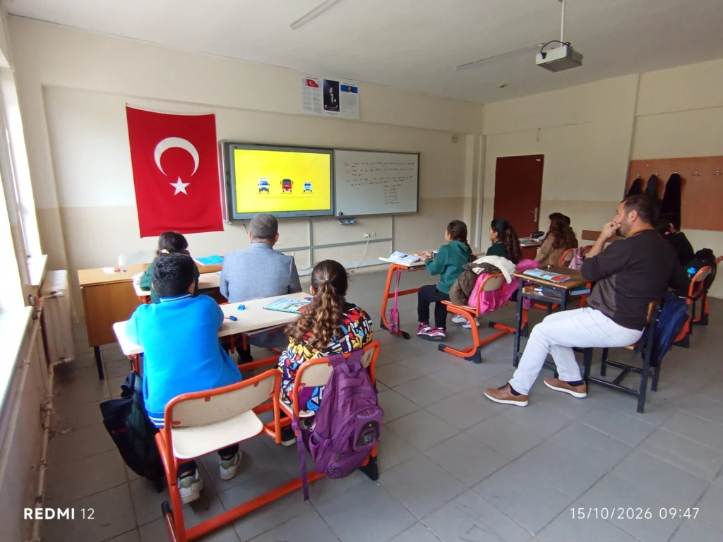 Öğrenciler sınıfta afet farkındalığı eğitimine katıldı.
Sınıfta öğrenciler ve eğitimciler akıllı tahtadaki sunumu izliyor.